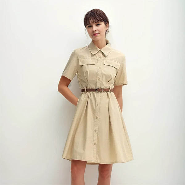 Femme portant une robe saharienne traditionnelle beige, manches courtes, ceinturée à la taille, dans un studio au fond blanc – look estival élégant et décontracté.
