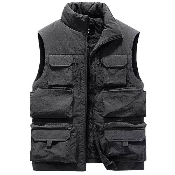 Veste sans manche de style saharienne en couleur grise foncée, équipée de nombreuses poches de tailles variées sur le devant pour une utilité maximale. La fermeture éclair robuste et le col montant offrent une isolation et une protection supplémentaires, rendant cette veste idéale pour des activités extérieures par temps froid.