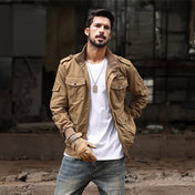 Un homme portant une veste de style baroudeur en couleur marron beige, debout dans un environnement urbain délabré. Il est habillé d'un t-shirt blanc et d'un jean, complétant son look aventureux avec des gants assortis. Sa posture confiante et son regard sérieux reflètent un style robuste et pratique, parfait pour un homme actif et stylé.