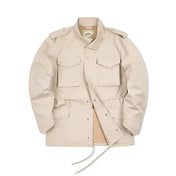 Veste pour homme de style saharienne en tissu beige, présentant un design classique avec quatre poches à rabat sur le devant et des épaulettes. La veste est fermée par des boutons pression visibles et équipée de cordons de serrage à la taille pour un ajustement personnalisé, mettant en avant une allure fonctionnelle et élégante.