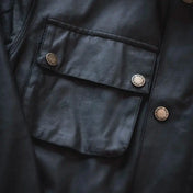 Détail d'une poche sur une veste saharienne homme Barbour noire, montrant les boutons gravés et le tissu de haute qualité, soulignant l'attention portée aux détails fins et pratiques de la veste.