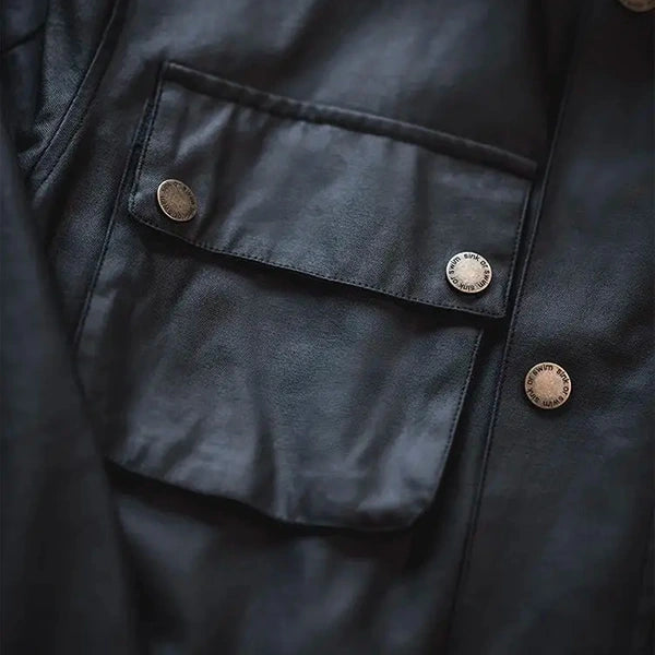 Détail d'une poche sur une veste saharienne homme Barbour noire, montrant les boutons gravés et le tissu de haute qualité, soulignant l'attention portée aux détails fins et pratiques de la veste.